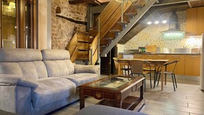 Un salon moderne avec un canapé, une table basse en verre et un coin repas comprenant des chaises, avec une cuisine en arrière-plan.
