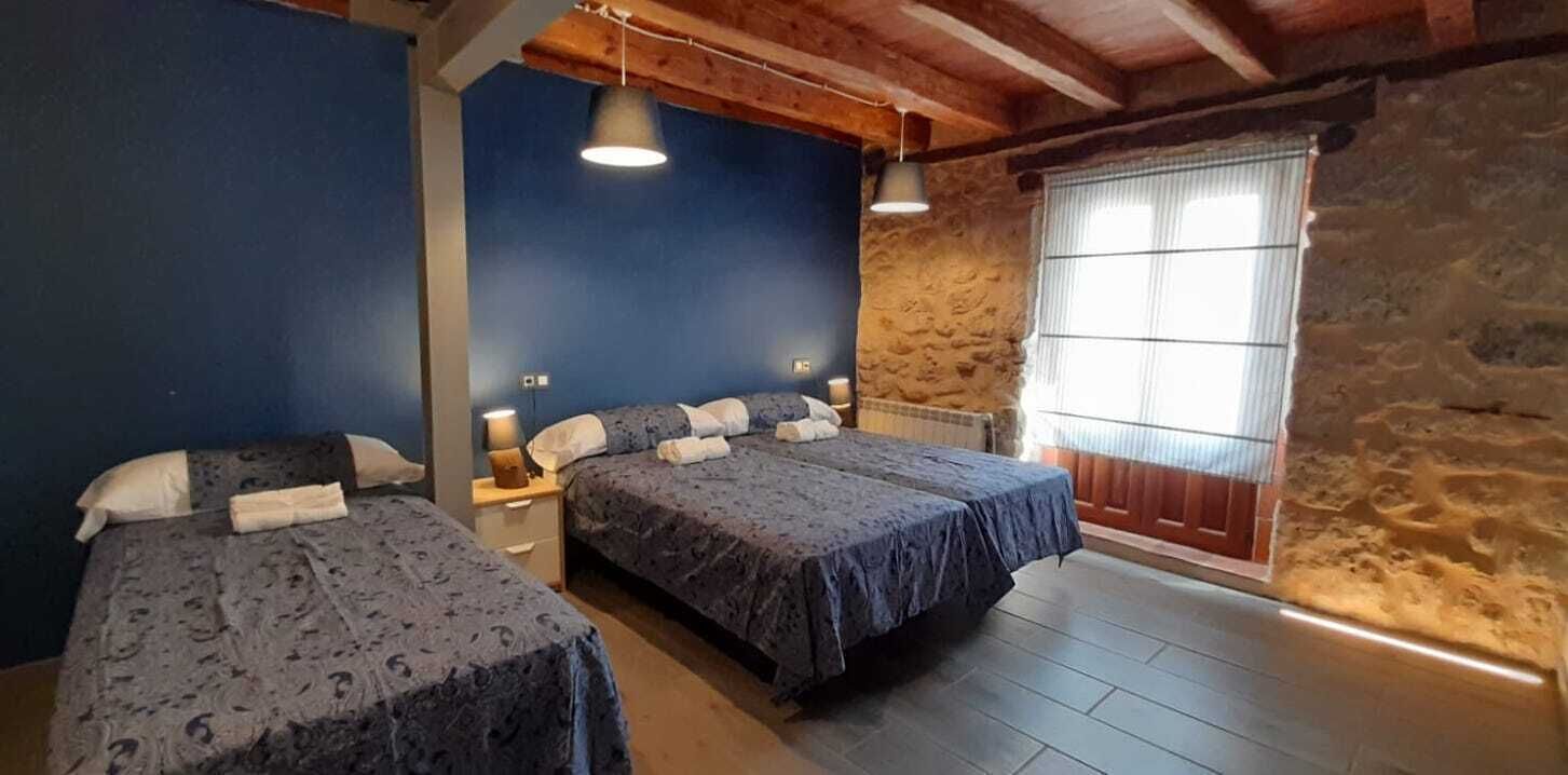 Una habitación con dos camas, una pared de piedra, techo de madera y una ventana con persianas.