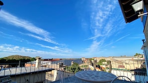 Une terrasse avec une table ronde et deux chaises, donnant sur un quartier résidentiel avec des maisons et une colline au loin.