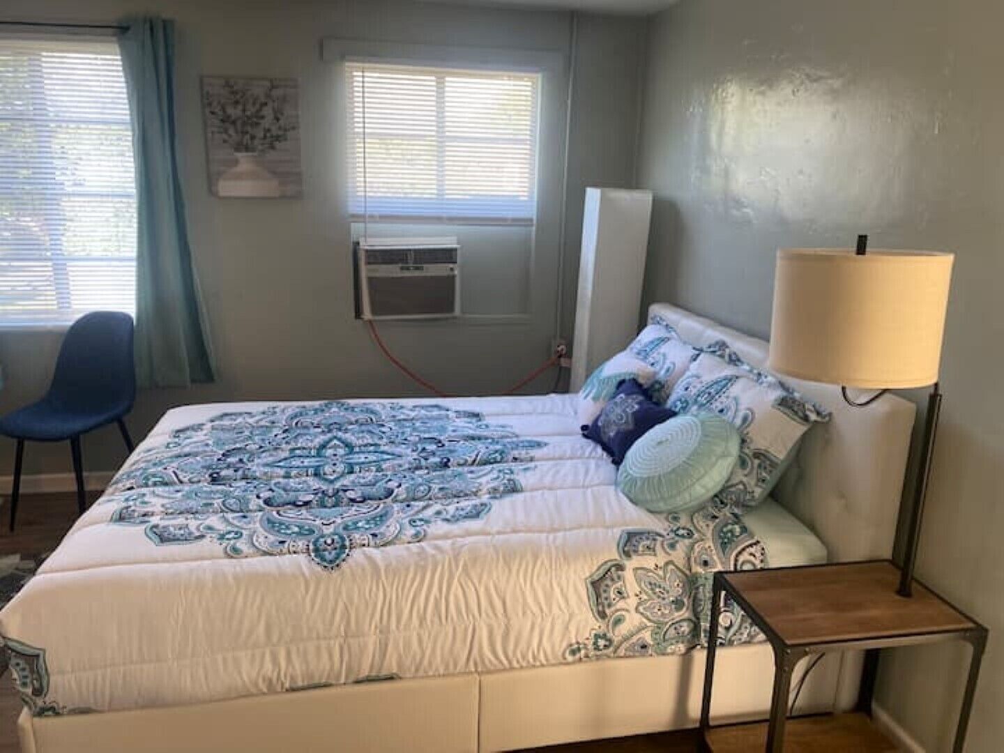 Un dormitorio con cama, una silla, una lámpara y un equipo de aire acondicionado.