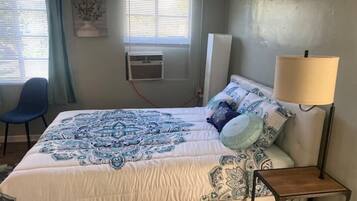 Un dormitorio con cama, una silla, una lámpara y un equipo de aire acondicionado.