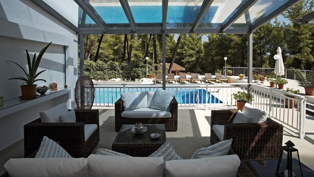 A glass-enclosed outdoor area with wicker furniture, a pool, and potted plants. - A Private Haven: Hera with Secluded Pool and Garden (Kassandra)
