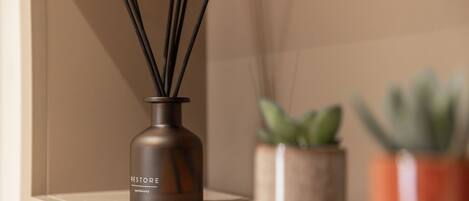 A bottle labeled 'RESTORE' with reed diffusers on a shelf, accompanied by two potted plants.