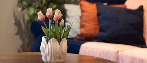A round wooden table with a white vase containing pink tulips.