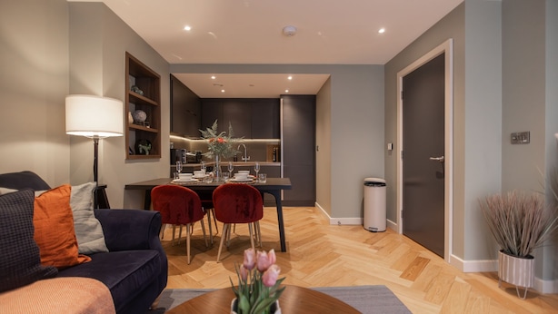 A modern living room with a sofa, a dining table with chairs, and a kitchen area in the background.
