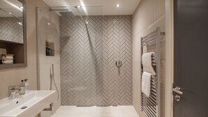 A modern bathroom with a herringbone tile backsplash, a glass-enclosed shower, and a vanity with a sink and towel rack.