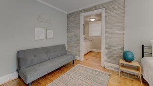 A modern bedroom with a grey sofa, a patterned rug, and a small table with a decorative item.