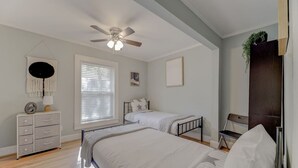 A bedroom with two beds, a ceiling fan, a dresser, and a window with blinds.