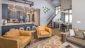 A modern kitchen with a bar area, a dining space, and a living area with leather sofas and a chessboard.
