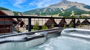 A hot tub with a mountain view, wooden cabins, and a clear sky.