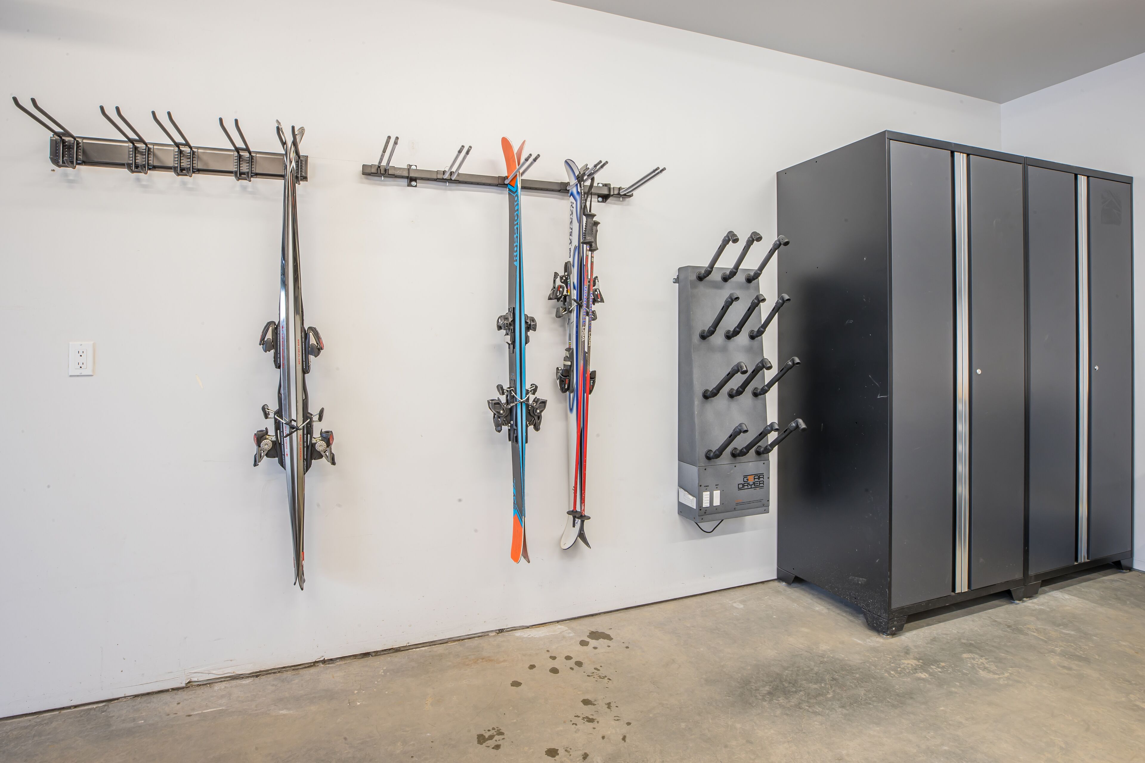 A ski storage area with multiple racks for skis and poles, a large black cabinet, and a concrete floor.