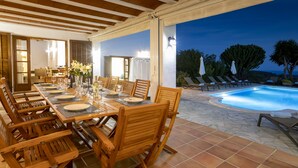 An outdoor dining area with a pool, wooden furniture, and a view of the pool at dusk.