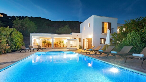 A swimming pool with lounge chairs, a building with a balcony, and a view of the surrounding landscape.