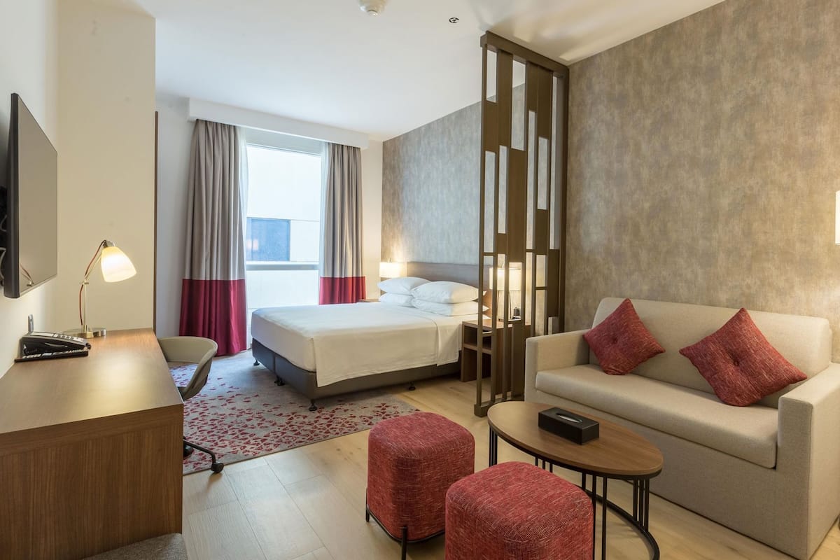 A hotel room with a bed, a sofa, a desk, a chair, and a small table.