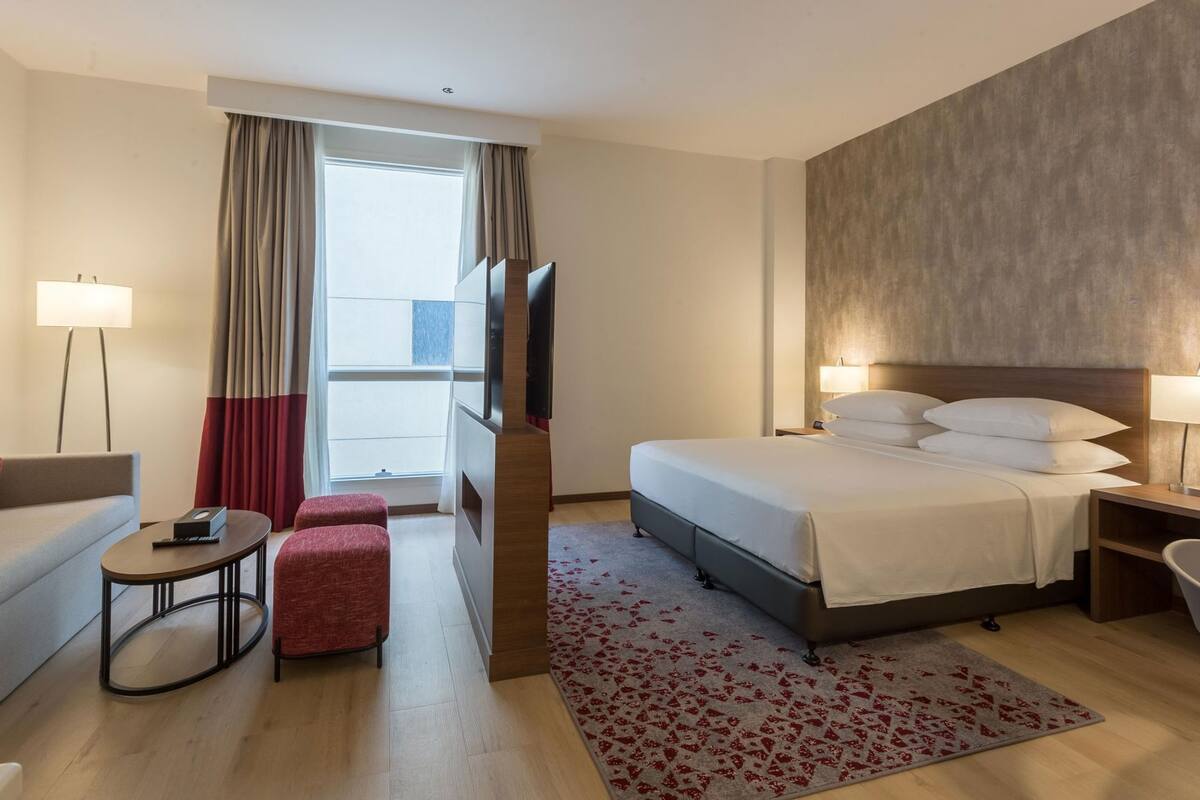 A hotel room with a bed, a sofa, a small table, a TV, and a bathroom.