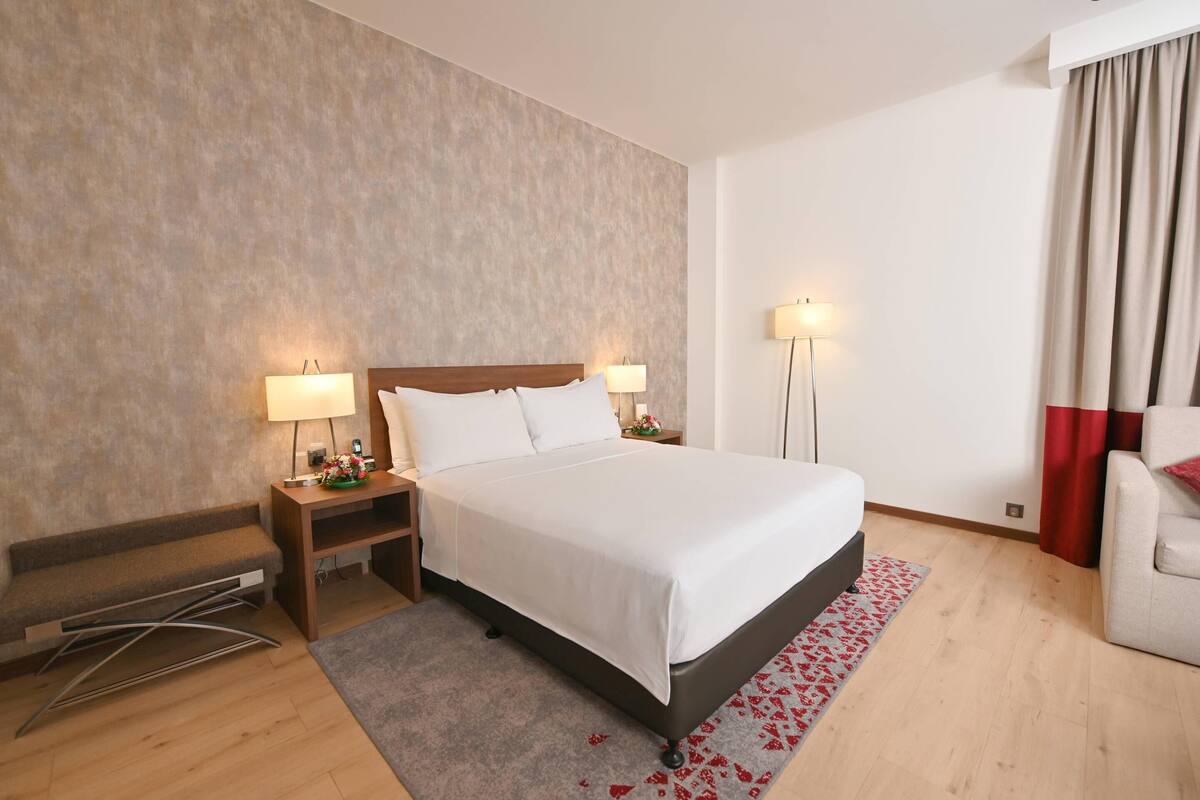 A hotel room with a bed, bedside tables, a bench, a desk, and a chair.