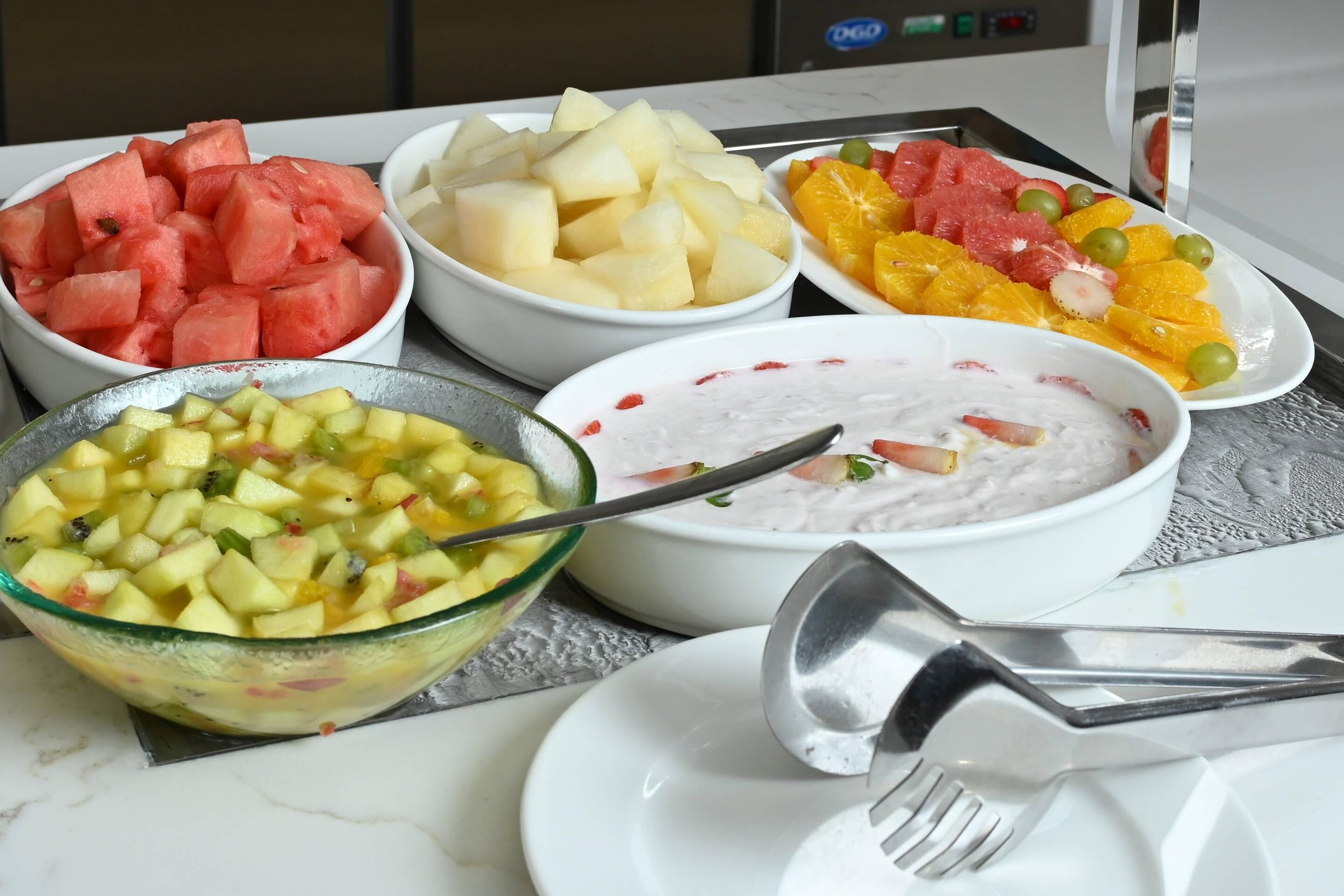 Una mesa con diferentes fuentes de fruta y un bol de ensalada de frutas.