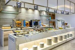 A buffet setup with various food items and utensils, a marble countertop, and overhead lighting.