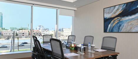 Un salón de conferencias con una gran mesa, seis sillas y vistas de la ciudad a través de amplios ventanales.