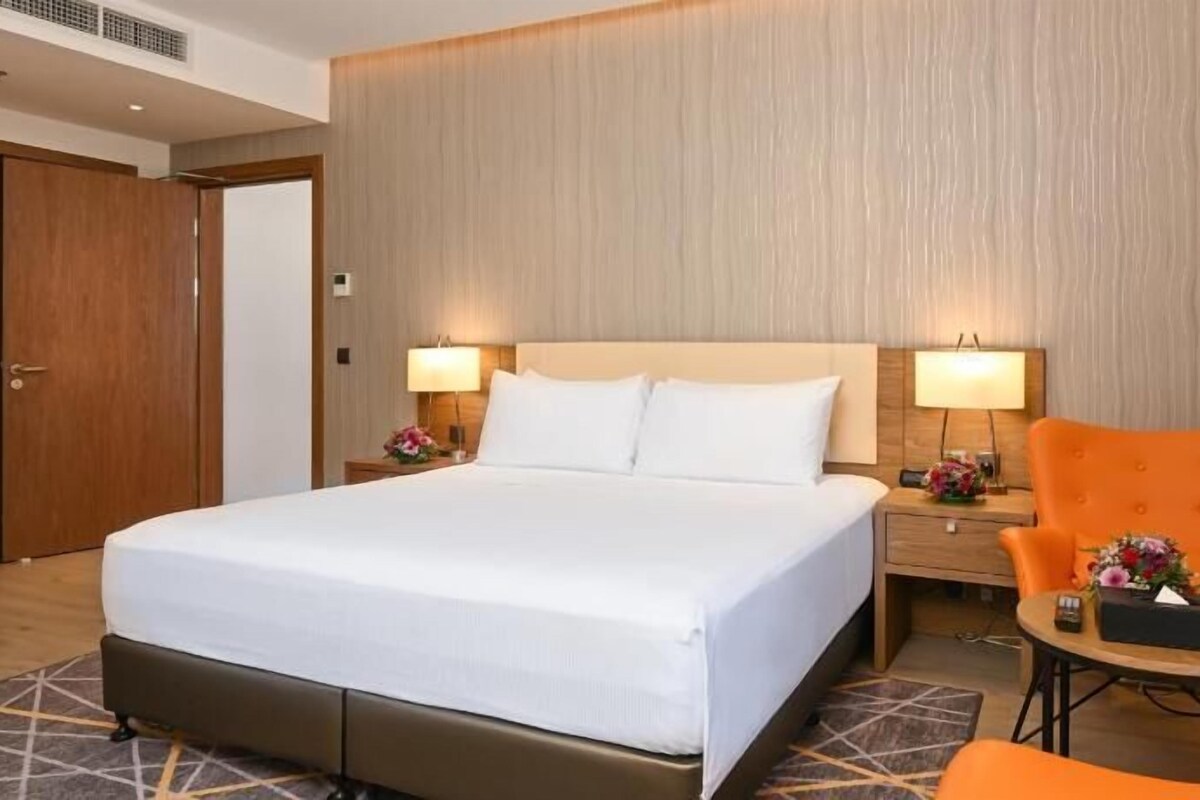 Ein Hotelzimmer mit einem großen Bett, zwei Nachttischen mit Lampen, einem Holzschrank und einem kleinen Tisch mit Stuhl.
