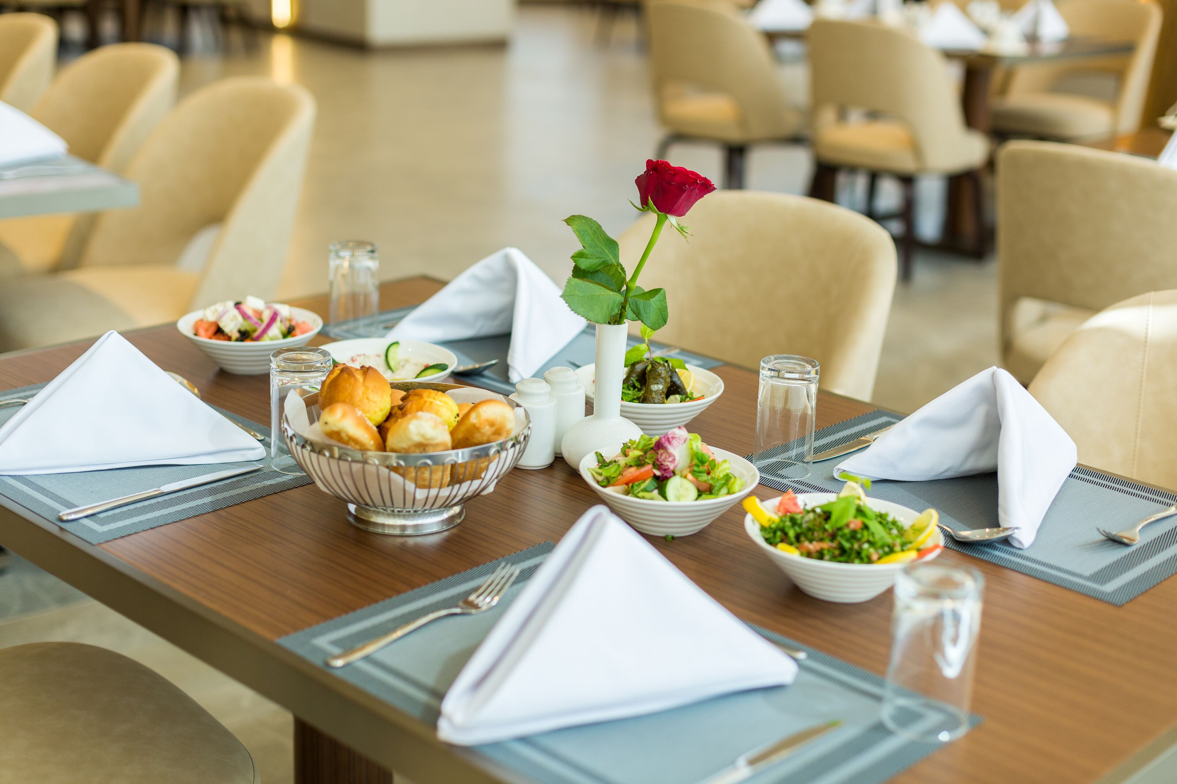 A dining table set with various dishes, a rose in a vase, and a bowl of bread.