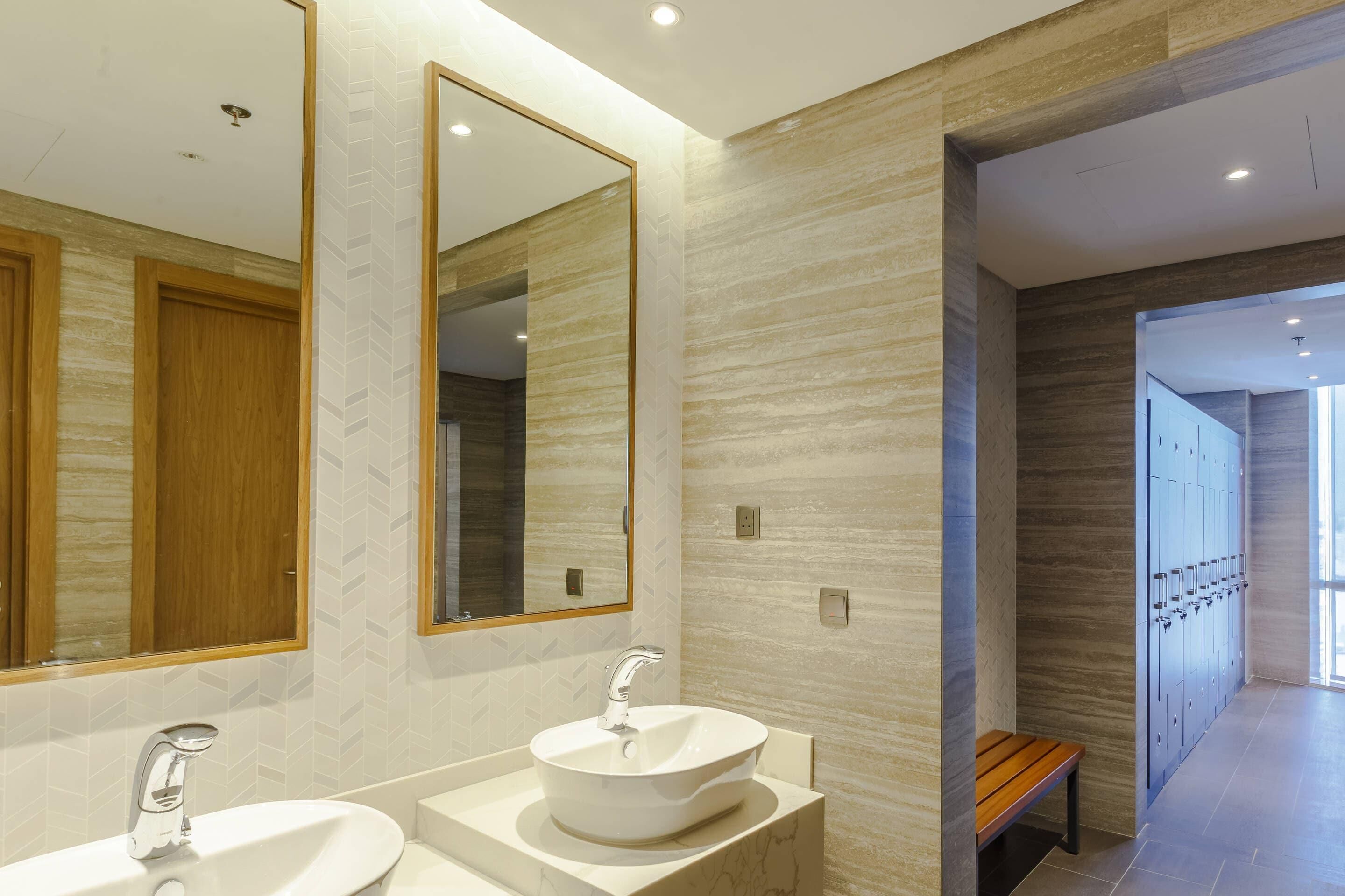 A modern bathroom with two sinks, a large mirror, and a wooden bench.