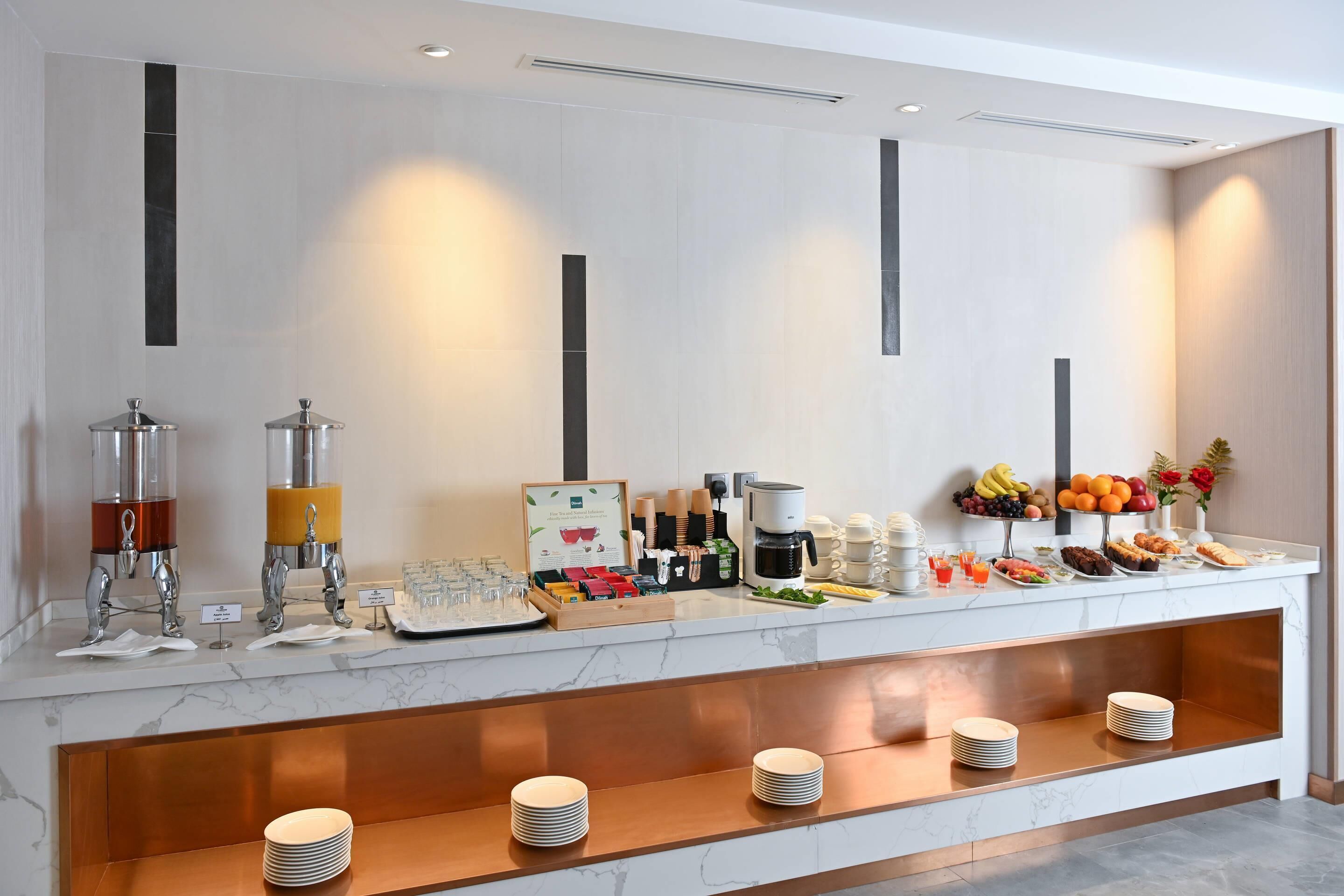A buffet setup with various food items and beverages, including fruits, pastries, and coffee.