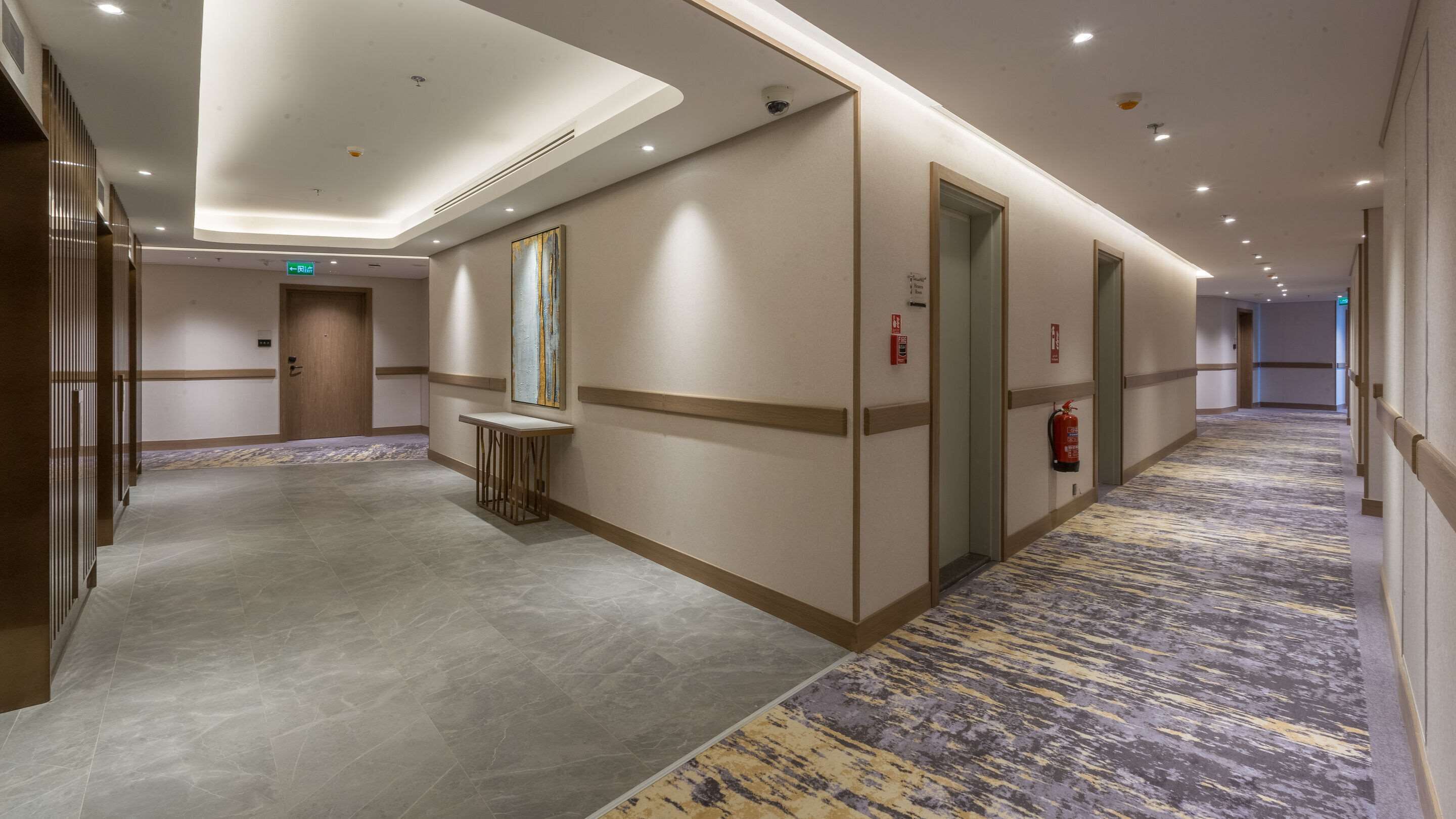 A hotel corridor with a marble floor, a small table, and a fire extinguisher.