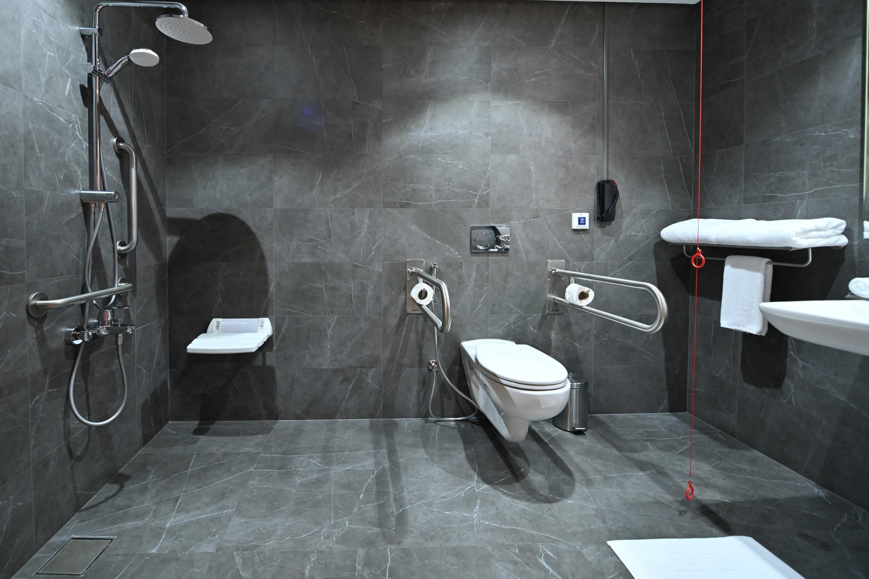 A modern bathroom with a shower, toilet, and sink, featuring marble walls and a tiled floor.