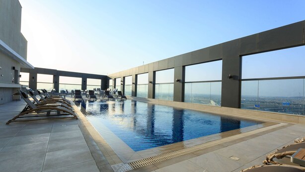 Una piscina infinita en la azotea con sillones de descanso y vistas despejadas del paisaje urbano.