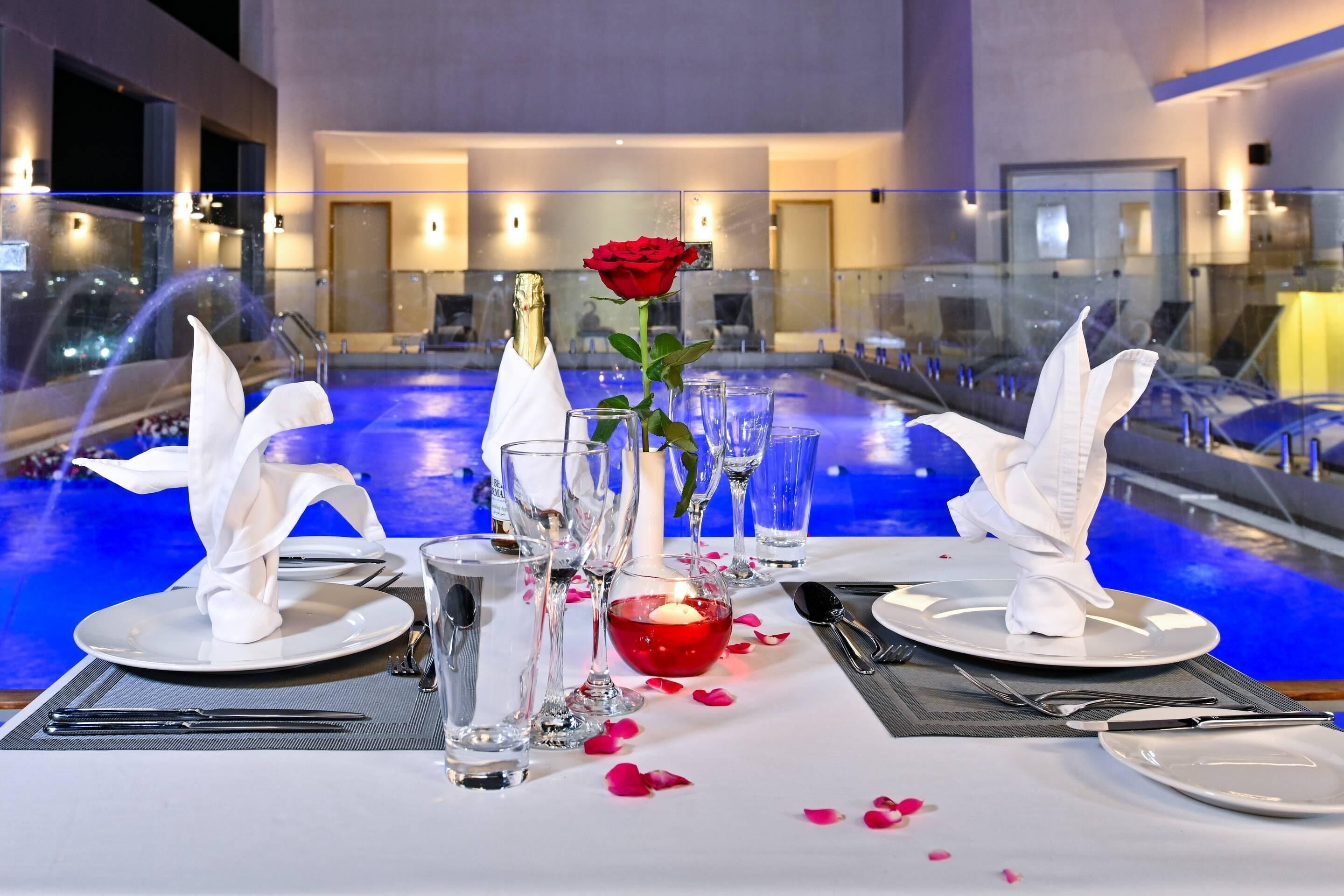 A dining table set with white napkins, a red rose, and a candle centerpiece.
