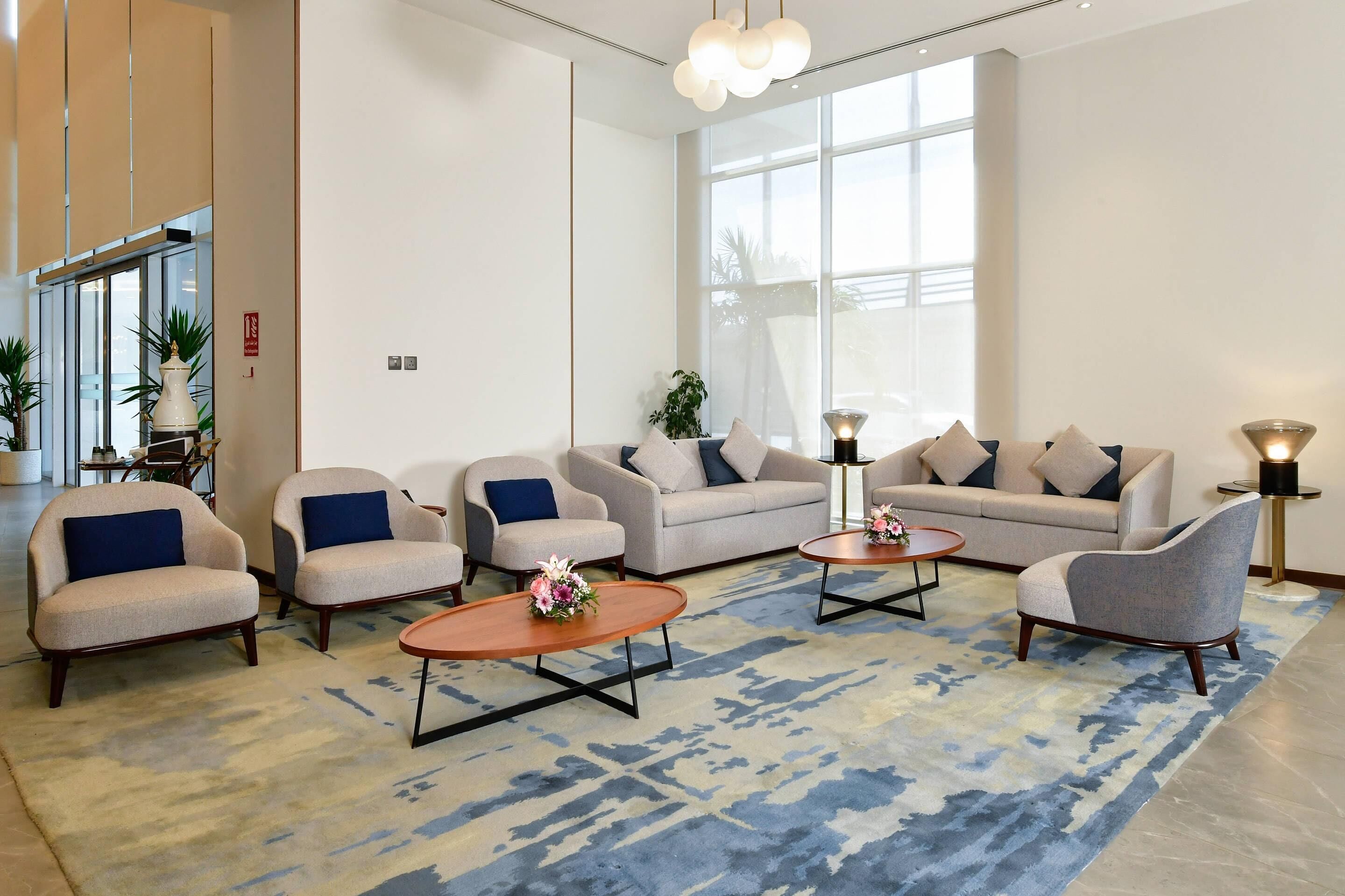 Un hall d’entrée moderne doté d’une grande fenêtre, de canapés, de fauteuils et d’un tapis à motifs.