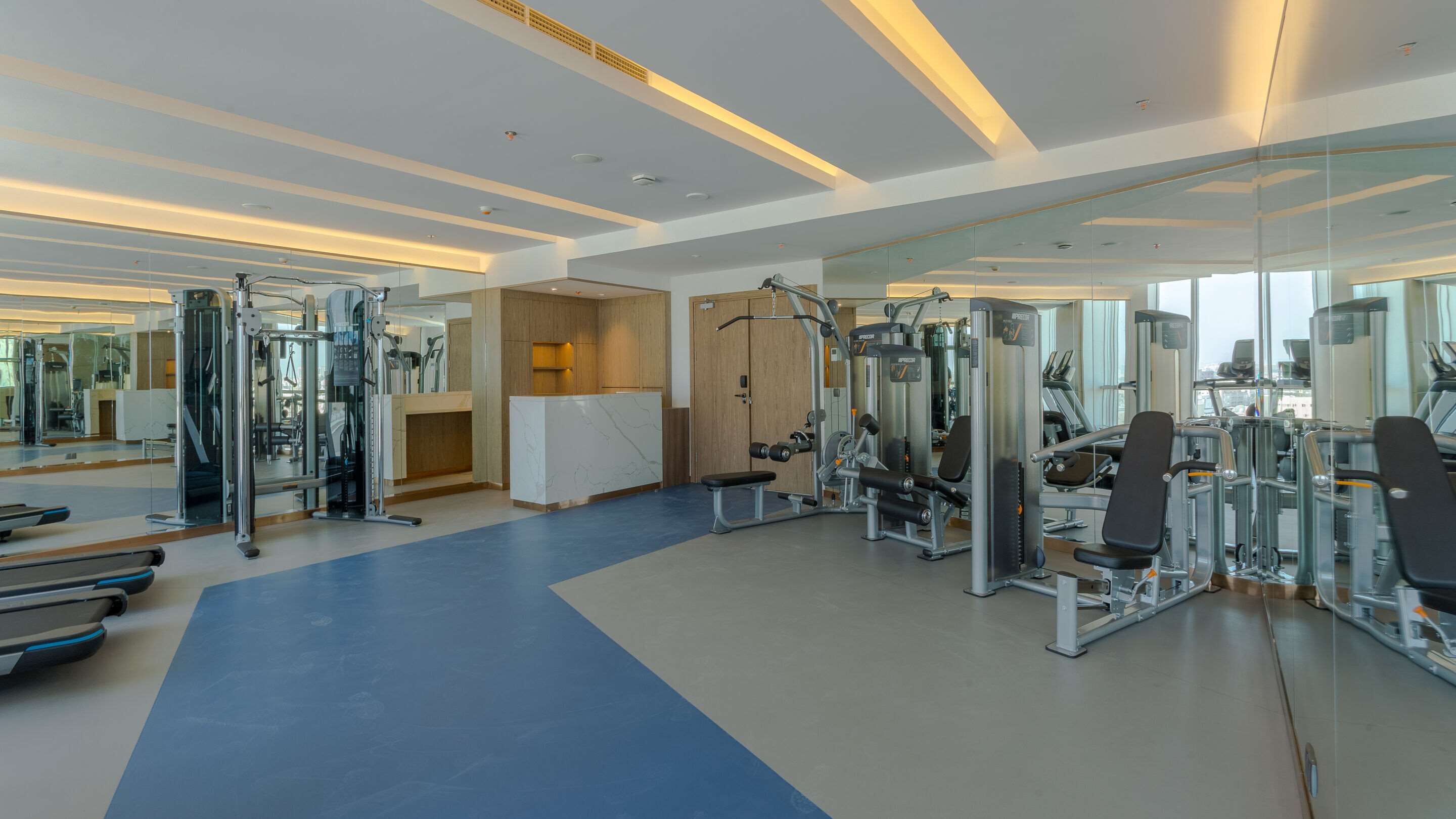 Un gimnasio moderno con diverso equipo de ejercicio, piso azul y espejos amplios.