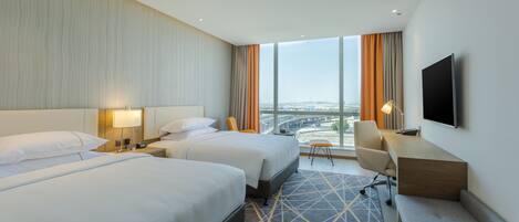 A hotel room with two beds, a desk, a chair, a TV, and a large window with a city view.