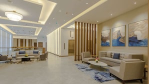 Un lobby espacioso con diseño moderno, que incluye un área de descanso con sofás y una mesa de centro, una escalera con paneles de madera y obras de arte en las paredes.
