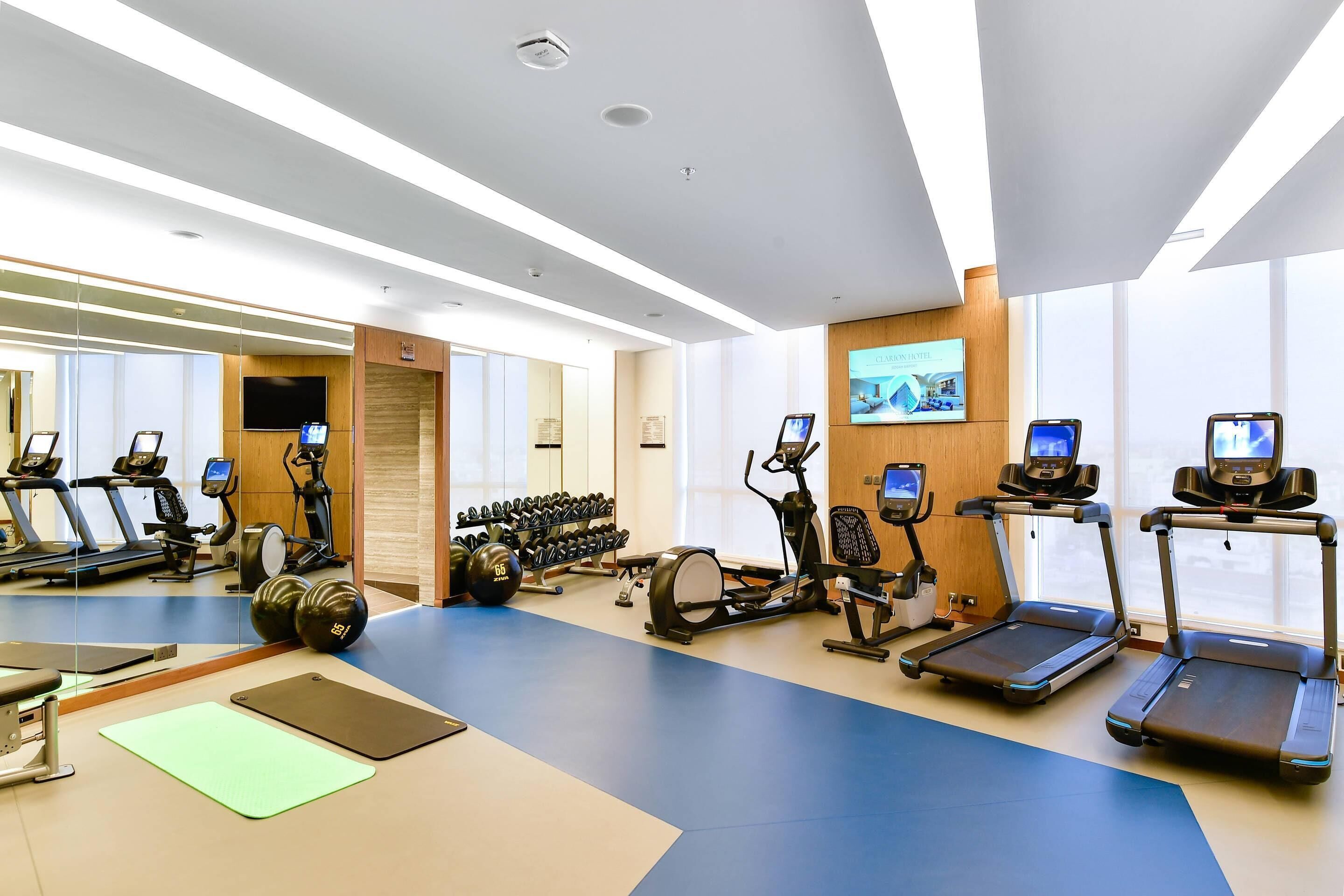 A modern gym with treadmills, elliptical machines, dumbbells, and exercise mats.