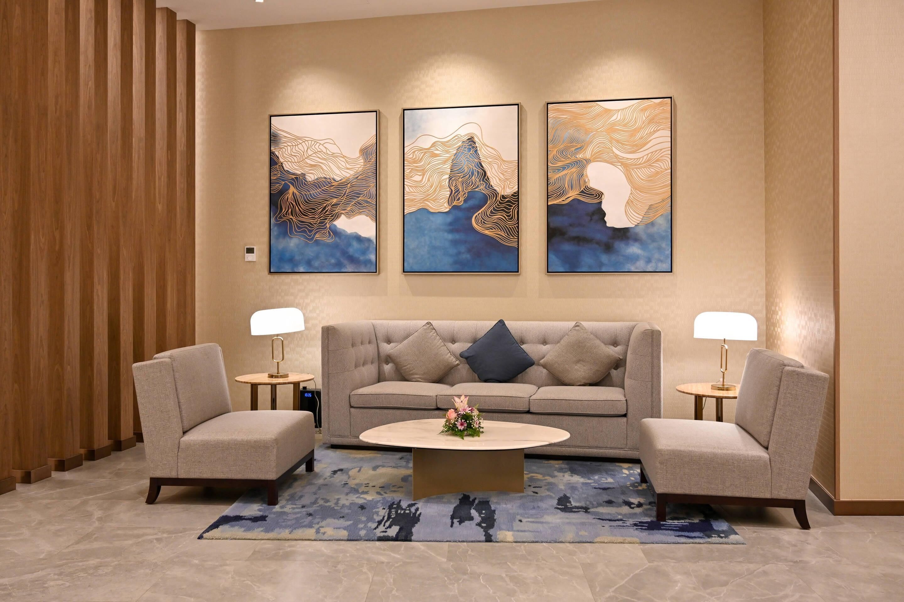 A modern lobby with a sofa, two armchairs, a coffee table, and three abstract wall art pieces.