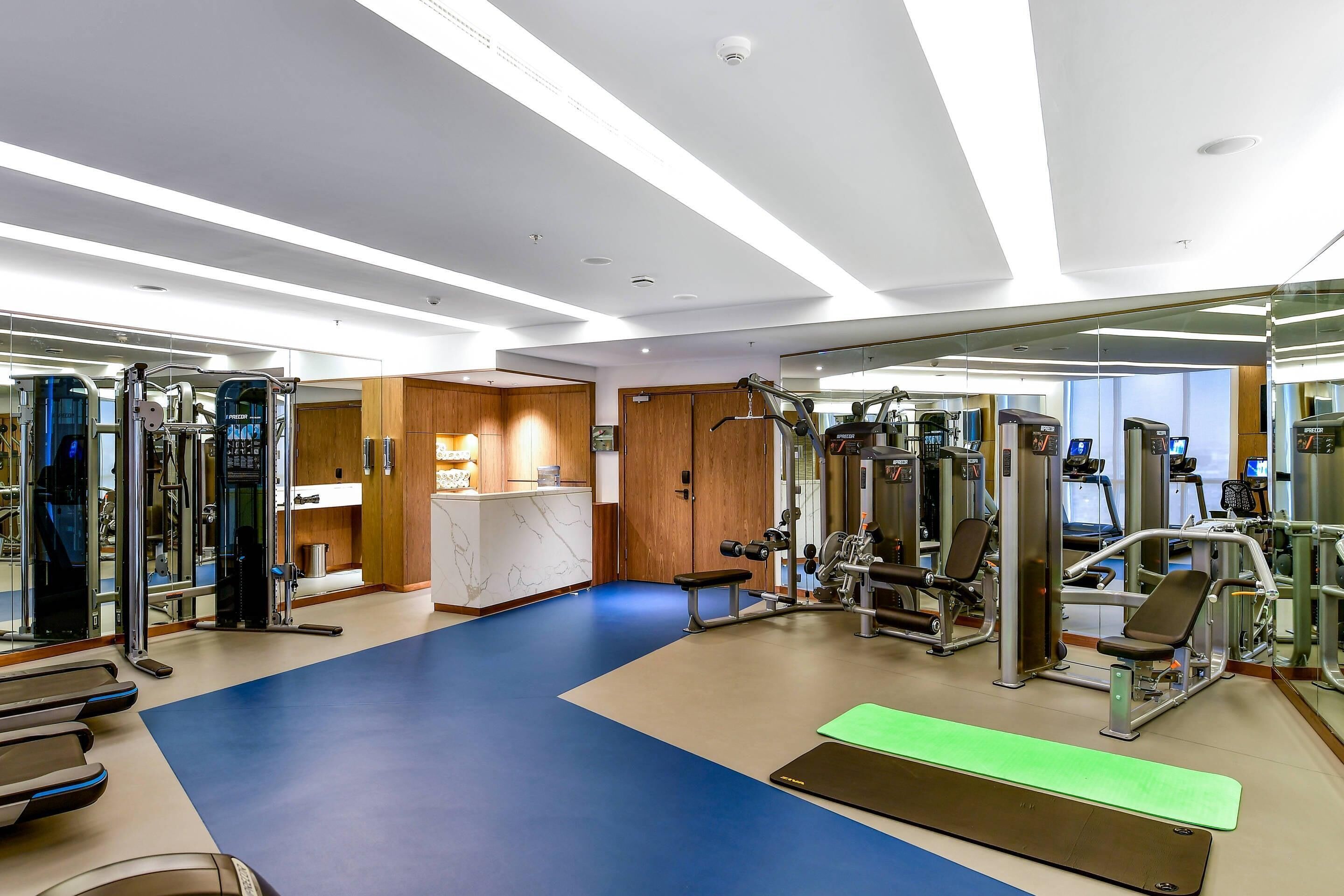A modern gym with various exercise equipment, a blue and beige floor, and a wooden reception desk.