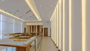 Un moderno vestíbulo de hotel con barandilla de vidrio, una escalera central y un largo pasillo con columnas.