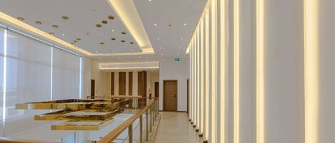 A modern hotel lobby with a glass railing, a central staircase, and a long corridor with columns.