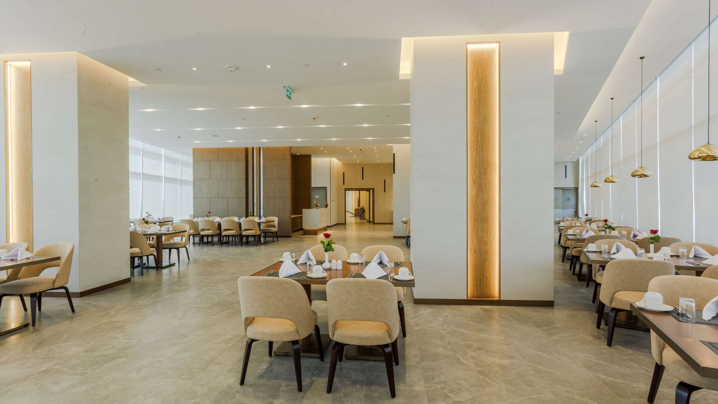 Un vaste espace de restauration d’hôtel, doté de nombreuses tables et chaises, d’un comptoir de réception central et d’un aménagement intérieur moderne.