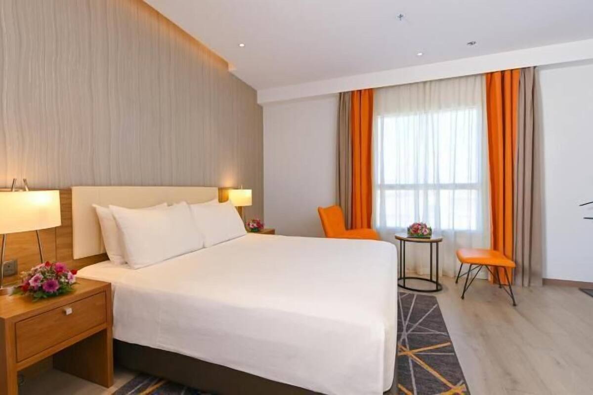 Une chambre d’hôtel comprenant un lit, des tables de chevet, un bureau, une chaise, une petite table et une fenêtre avec des rideaux.