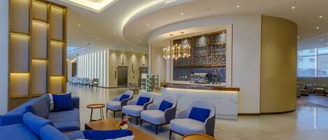 A modern lobby with sofas and armchairs, a reception desk, and a coffee bar.