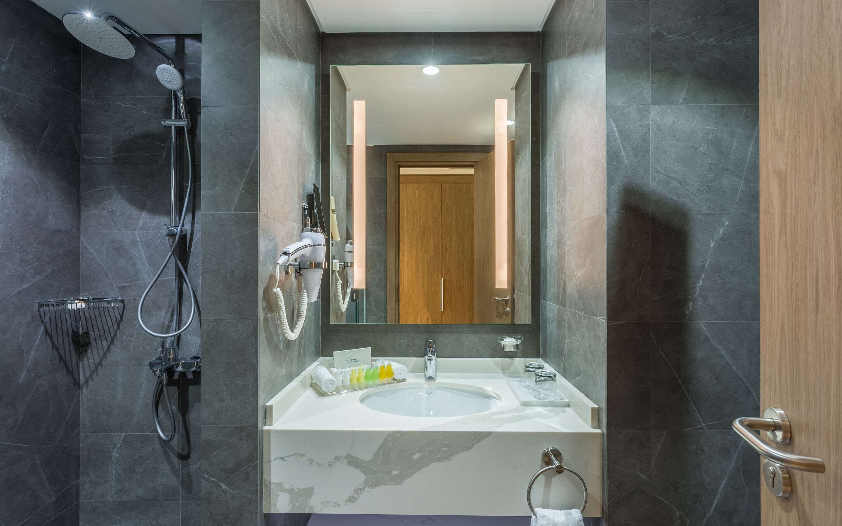 A modern bathroom with a large mirror, a shower, and a sink with toiletries.