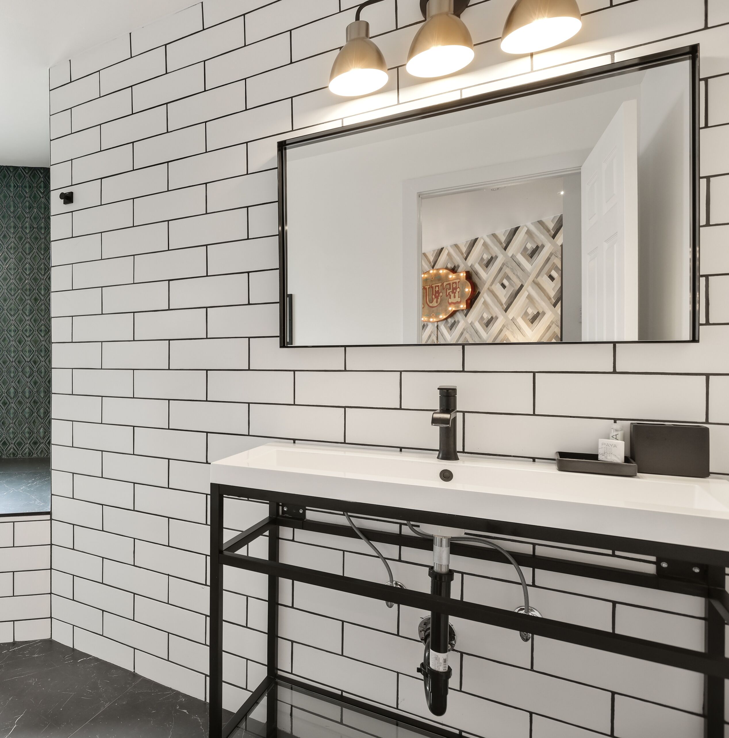 A bathroom with a white tiled wall, a black-framed sink, and a mirror above it.