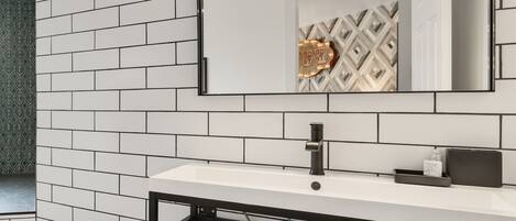 A bathroom with a white tiled wall, a black-framed sink, and a mirror above it.
