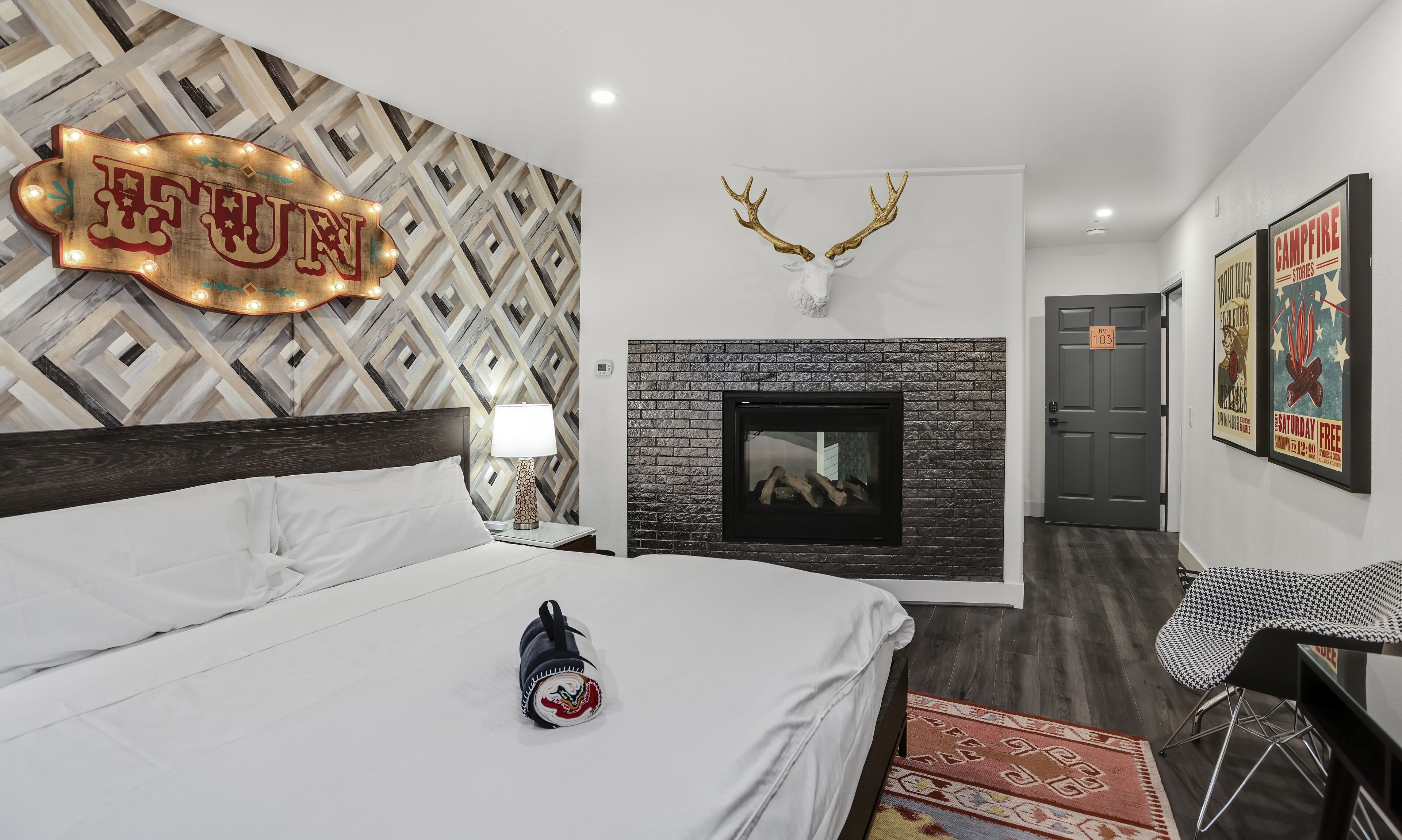 A modern hotel room with a bed, a fireplace, a wall-mounted deer head, and a sign reading "The Future."
