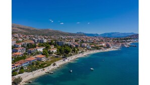 A coastal town with a beach, buildings, and mountains in the background. - Fantastic beachfront apartment with private balcony on the Adriatic.Top location (Seget Donji)