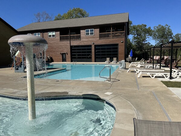 A swimming pool with a water feature, lounge chairs, and a building with a garage in the background. - Crown Jewel | Table Rock Lake Views | Sleeps 24 | Near Silver Dollar City (Indian Point)