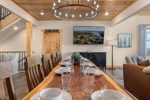 A dining area with a long wooden table set for a meal, a chandelier, and a view of a lakeside property. - Crown Jewel / Table Rock Lake Views / Near Silver Dollar City / NEWLY REMODELED (Indian Point)